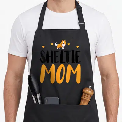 Tablier de cuisine noir avec inscription Sheltie Mom et dessin chien de berger Shetland aux couleurs orange et blanc.