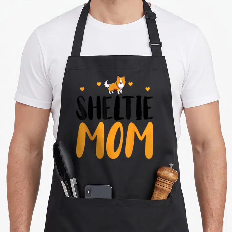 Tablier de cuisine noir avec inscription Sheltie Mom et dessin chien de berger Shetland aux couleurs orange et blanc.