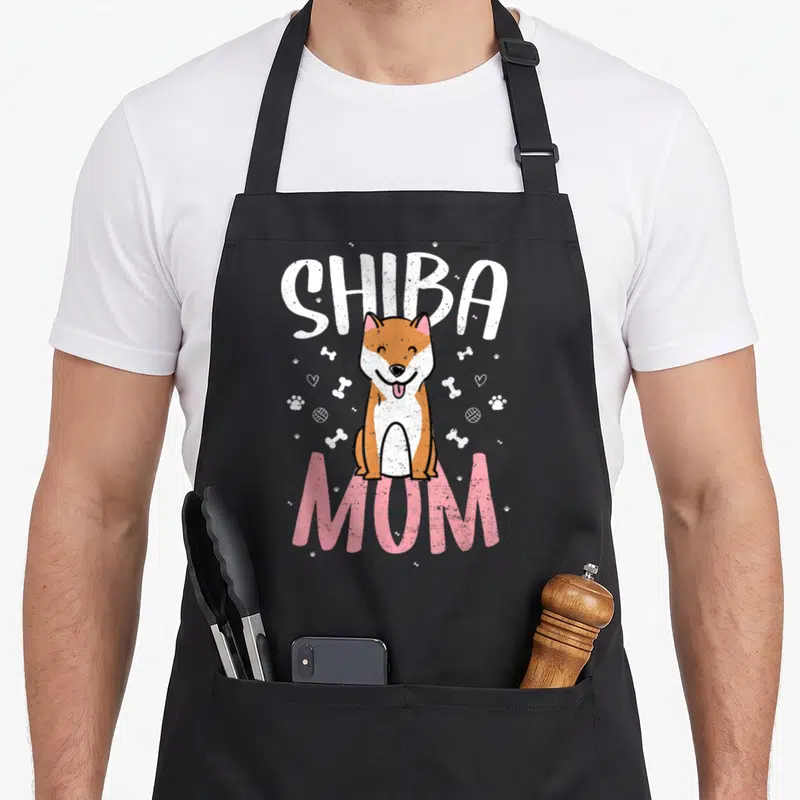 Tablier de cuisine noir avec illustration d'un Shiba Inu souriant et les mots Shiba Mom en lettres blanches et roses.
