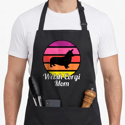 Tablier de cuisine noir avec silhouette corgi gallois et texte Welsh Corgi Mom sur fond de soleil coloré.