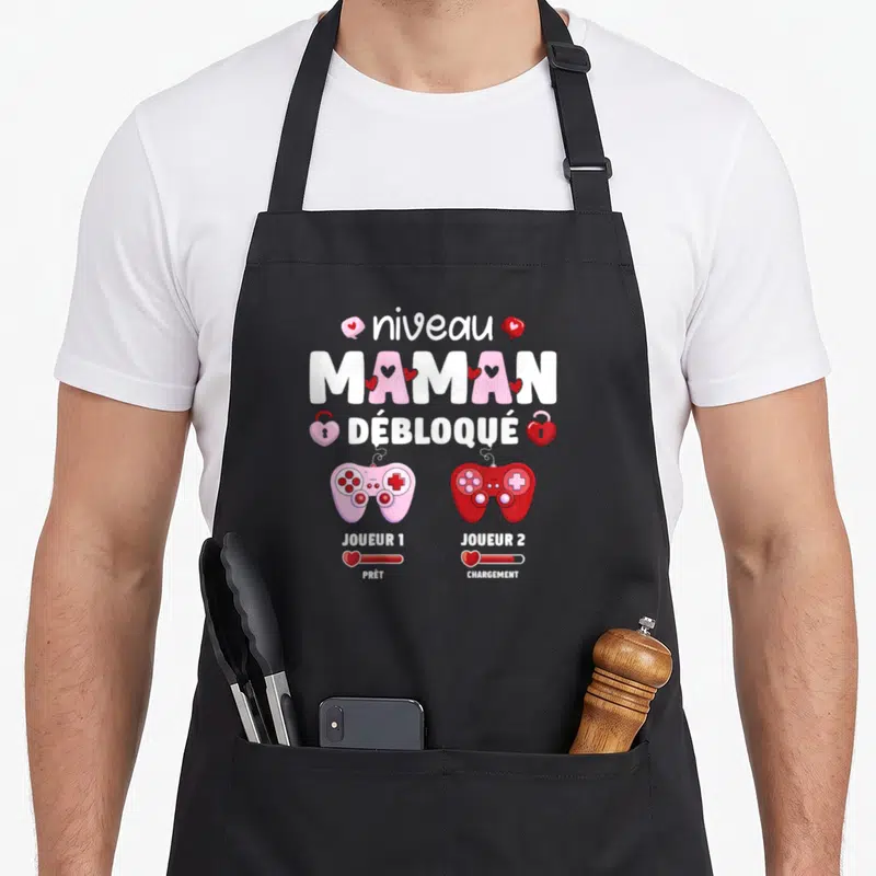 Tablier de cuisine noir avec illustration manettes rose et rouge et texte niveau maman débloqué joueur 1 prêt joueur 2 chargement