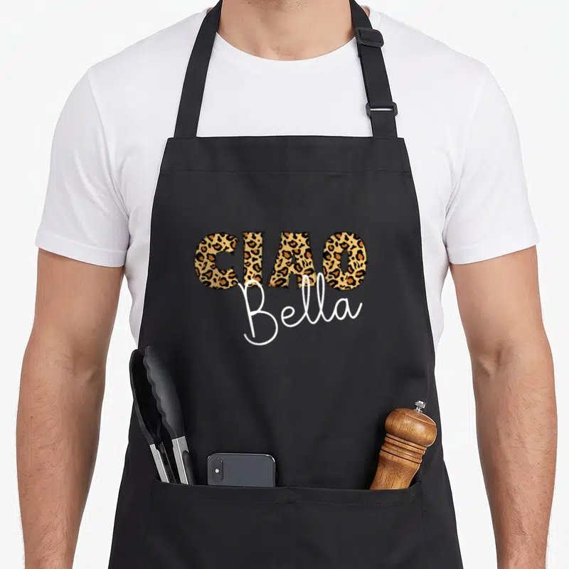 Tablier de cuisine noir avec inscription Ciao Bella en lettres à motif léopard et script blanc élégant.