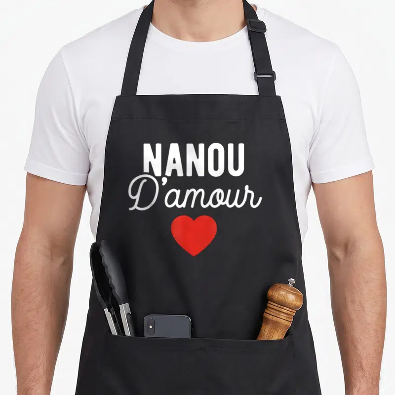 Tablier de cuisine noir avec l'inscription Nanou D'amour en blanc et un cœur rouge au centre.