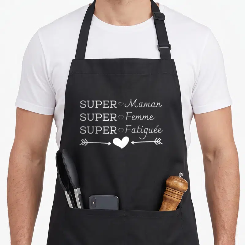 Tablier de cuisine noir avec inscription blanche super maman super femme super fatiguée et motifs de cœurs et flèches.