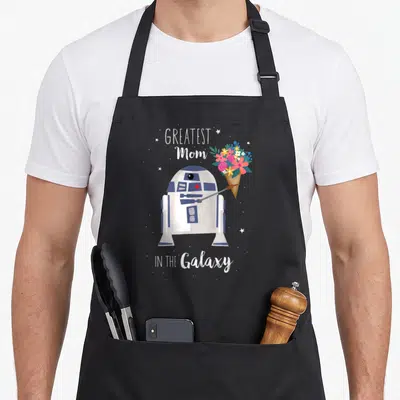 Tablier de cuisine noir avec R2-D2 tenant un cône de fleurs et le texte Greatest Mom in the Galaxy.