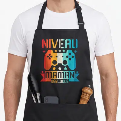 Tablier de cuisine noir avec illustration manette de jeu vidéo multicolore et texte Niveau Maman Débloqué.