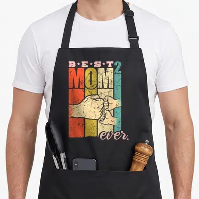Tablier de cuisine noir avec inscription Best Mom 2 et illustration vintage de mains jointes sur fond rayé coloré.