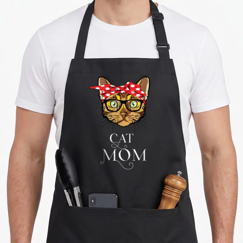 Tablier de cuisine noir avec tête de chat au bandana rouge à pois et texte Cat Mom en blanc.