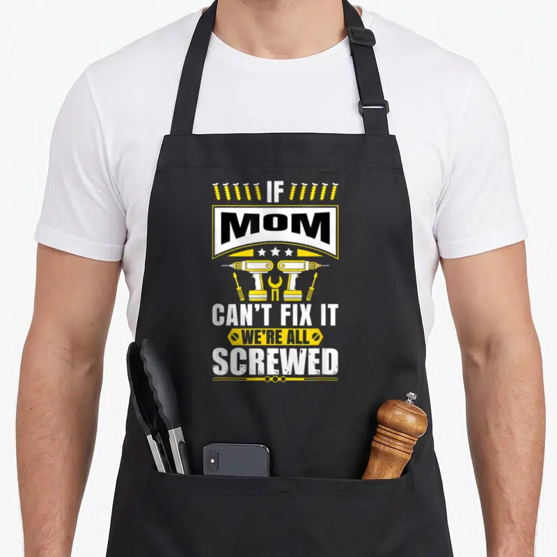 Tablier de cuisine noir avec illustration jaune et blanche de perceuses, vis et texte anglais sur la compétence de maman.