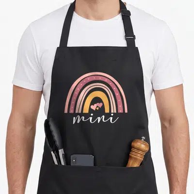 Tablier de cuisine noir avec arc-en-ciel pastel et inscription mini accompagnée de trois cœurs roses.