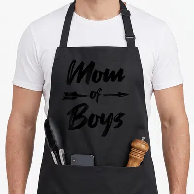 Tablier de cuisine noir avec l'inscription Mom of Boys traversée par une flèche noire directionnelle.