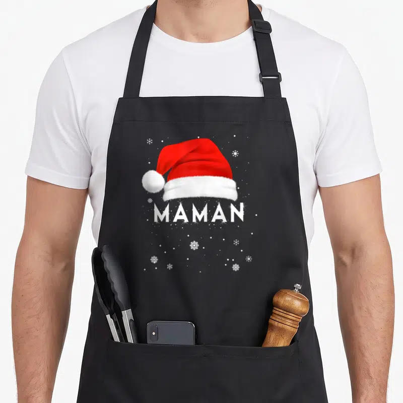 Tablier de cuisine noir avec un bonnet de Père Noël rouge et le mot MAMAN en blanc entouré de flocons de neige.
