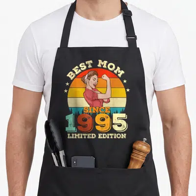Tablier de cuisine noir avec illustration vintage d'une femme musclée et texte Best Mom Since 1995 Limited Edition sur fond de soleil arc-en-ciel.