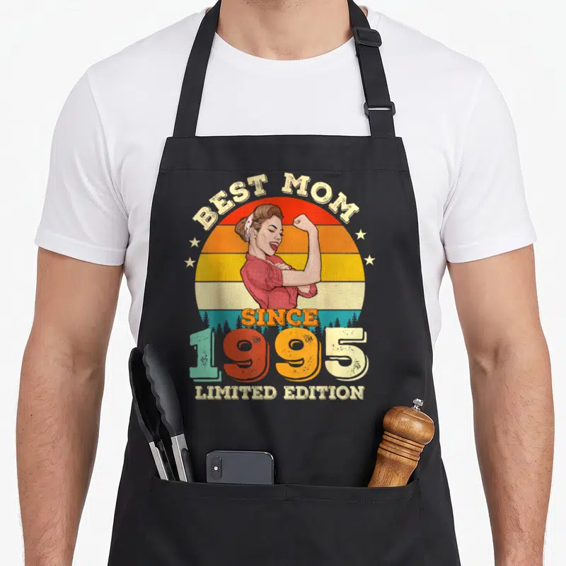 Tablier de cuisine noir avec illustration vintage d'une femme musclée et texte Best Mom Since 1995 Limited Edition sur fond de soleil arc-en-ciel.