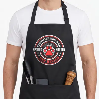 Tablier de cuisine noir avec logo circulaire rouge et blanc mentionnant Certified Dog Mom Spoiled Rotten Red Heeler au centre.