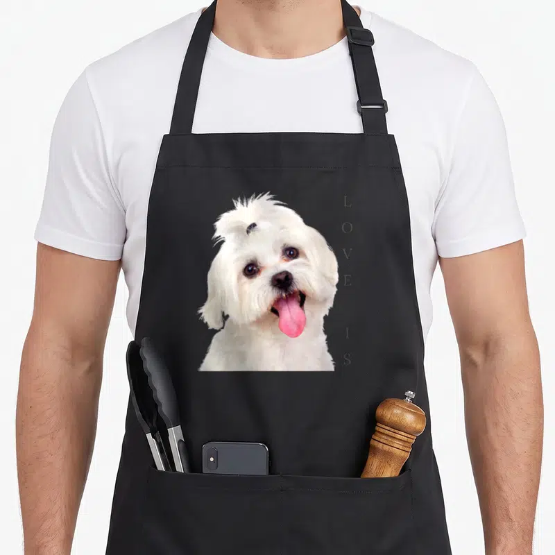 Tablier de cuisine noir avec portrait de bichon maltais blanc et texte vertical gris LOVESIS sur le côté droit.