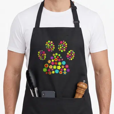 Tablier de cuisine noir avec une patte de chien formée de fleurs colorées vives sur fond uni.