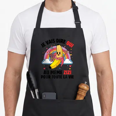 Tablier de cuisine noir avec une banane rose tenant des fleurs et le texte Je vais dire oui au même zizi pour toute la vie