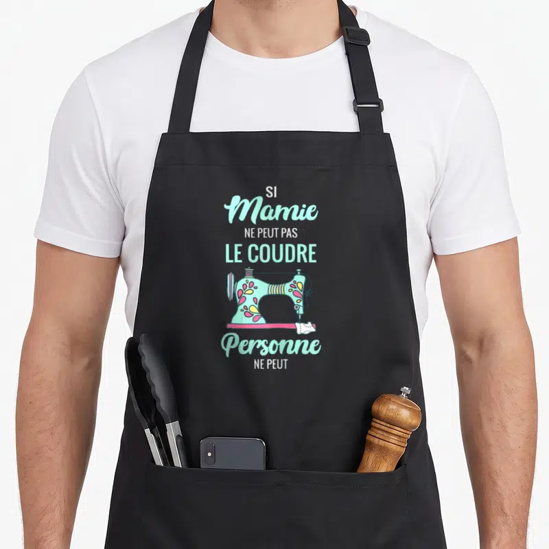 Tablier de cuisine noir avec une machine à coudre pastel et le texte Si Mamie ne peut pas le coudre personne ne peut.