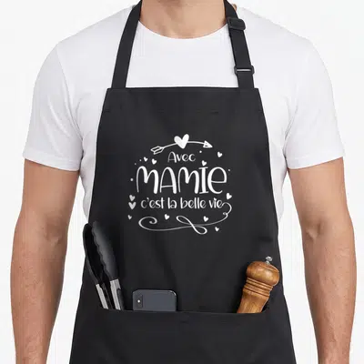 Tablier de cuisine noir avec inscription blanche Avec Mamie c'est la belle vie entourée de petits coeurs et d'une flèche.