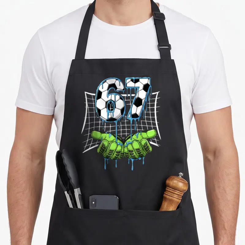 Tablier de cuisine noir avec les chiffres 67 en motif de ballon de football et des gants de gardien de but verts.