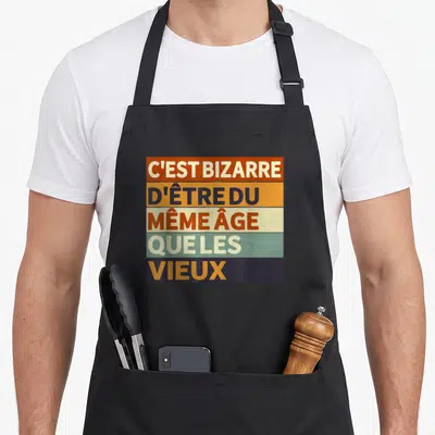 Tablier de cuisine noir avec inscription colorée c'est bizarre d'être du même âge que les vieux sur fond de bandes horizontales.