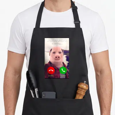 Tablier de cuisine noir avec l'image d'un appel entrant de John Pork le porc en chemise à carreaux.