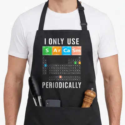 Tablier de cuisine noir avec le tableau périodique des sarcasmes et les mots I Only Use Sarcasm Periodically imprimés en blanc et couleurs vives.