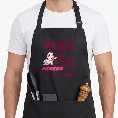Tablier de cuisine noir avec inscription Mamie en 2022 et illustration d'un bébé riant.
