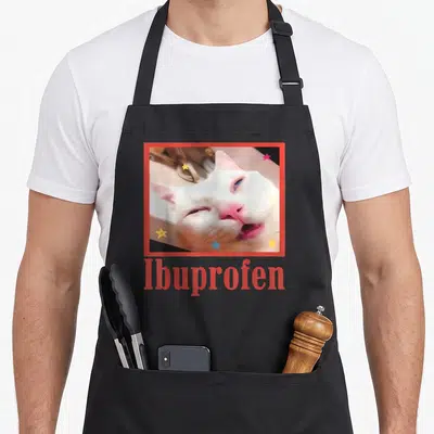 Tablier de cuisine noir avec photo d'un chat blanc et le mot Ibuprofen en rouge encadré de étoiles colorées.