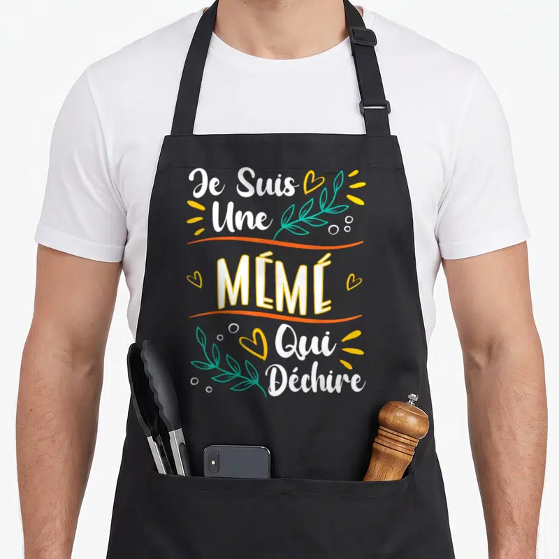Tablier de cuisine noir avec l'inscription Je Suis Une Mémé Qui Déchire en blanc et jaune, orné de cœurs et de feuilles vertes.