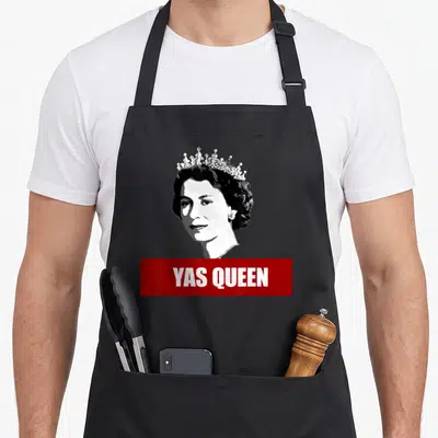 Tablier de cuisine noir avec portrait stylisé d'une reine coiffée et bandeau rouge Yas Queen en bas.