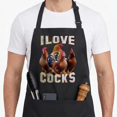 Tablier de cuisine noir avec trois coqs illustrés et le texte I Love Cocks en lettres capitales décorées.