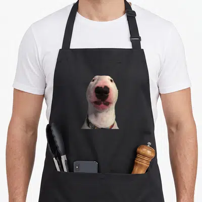 Tablier de cuisine noir avec la tête du chien blanc Walter au nez rose et collier coloré imprimé au centre.