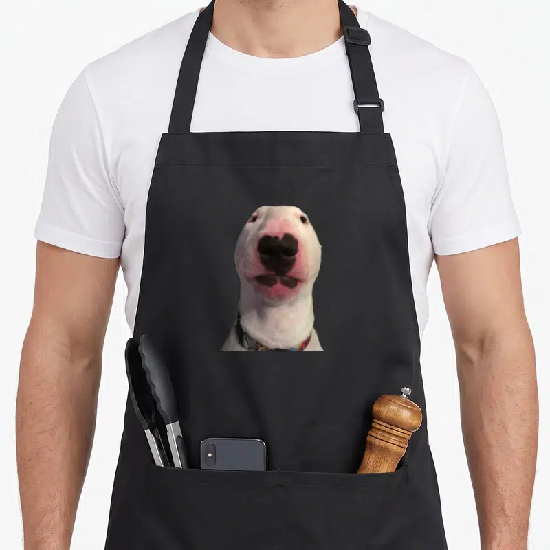 Tablier de cuisine noir avec la tête du chien blanc Walter au nez rose et collier coloré imprimé au centre.