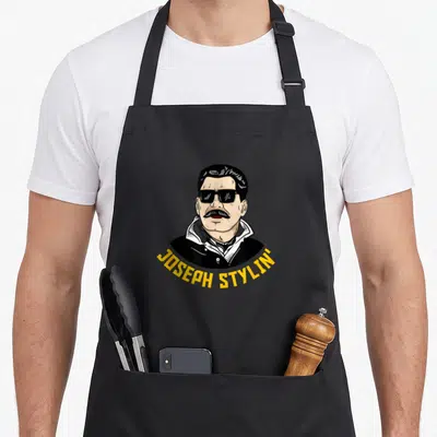 Tablier de cuisine noir avec illustration de Joseph Stylin' portant des lunettes noires et une chemise à col.
