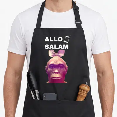 Tablier de cuisine noir avec un singe portant une paillette rose et le texte Allo Salam en haut.