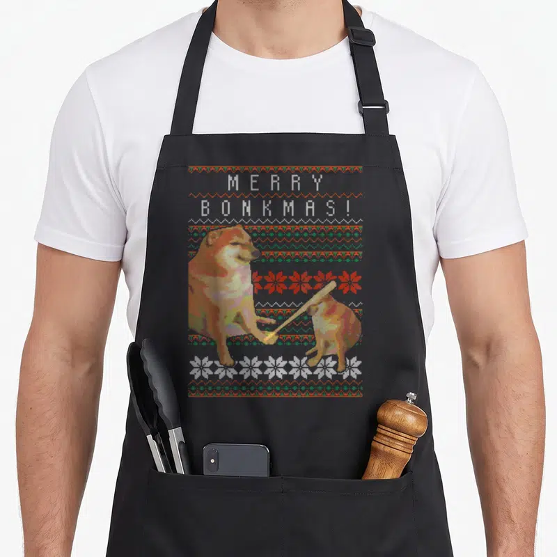 Tablier de cuisine noir avec illustration pixelisée de deux chiens Shiba Inu et le texte Merry Bonkmas sur un motif de tricot festif.
