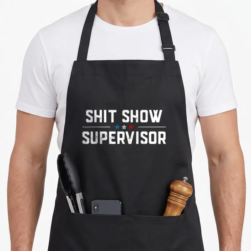 Tablier de cuisine noir avec l'inscription Shit Show Supervisor en blanc et trois étoiles bleue, blanche et rouge.