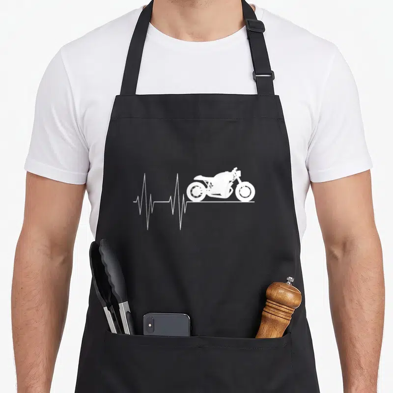Tablier de cuisine noir avec silhouette moto blanche et ligne de rythme cardiaque stylisée sur fond uni.