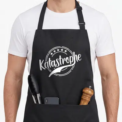 Tablier de cuisine noir avec l inscription Katastrophe et un dessin de vis blanche au centre d un cercle décoratif.