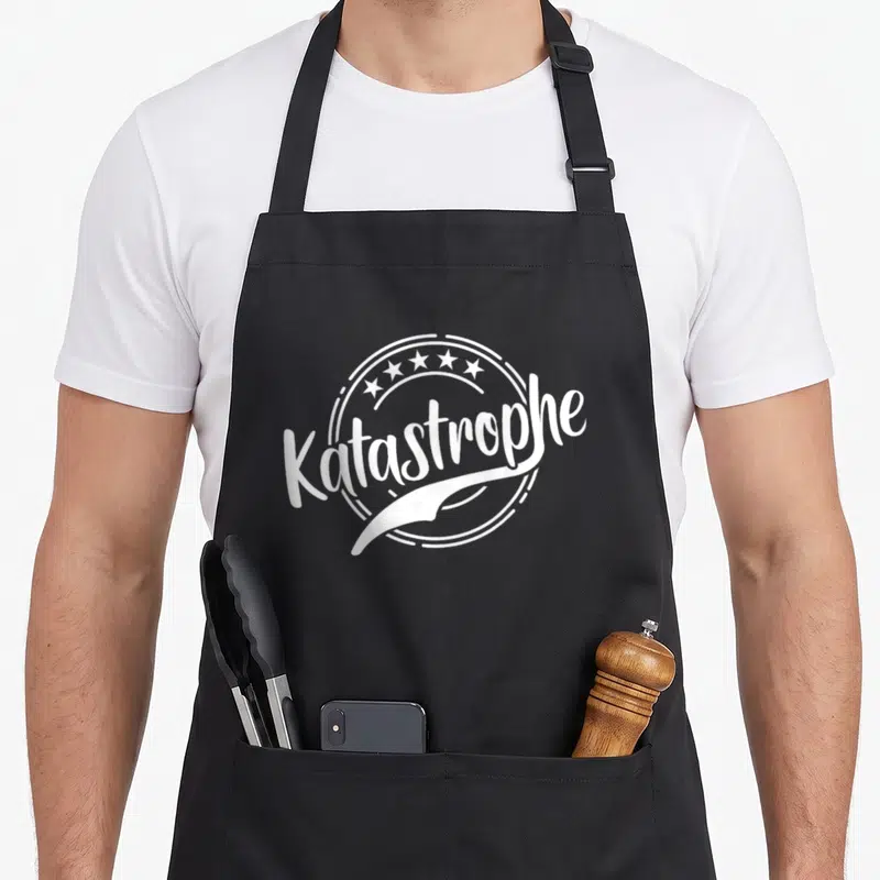 Tablier de cuisine noir avec l inscription Katastrophe et un dessin de vis blanche au centre d un cercle décoratif.