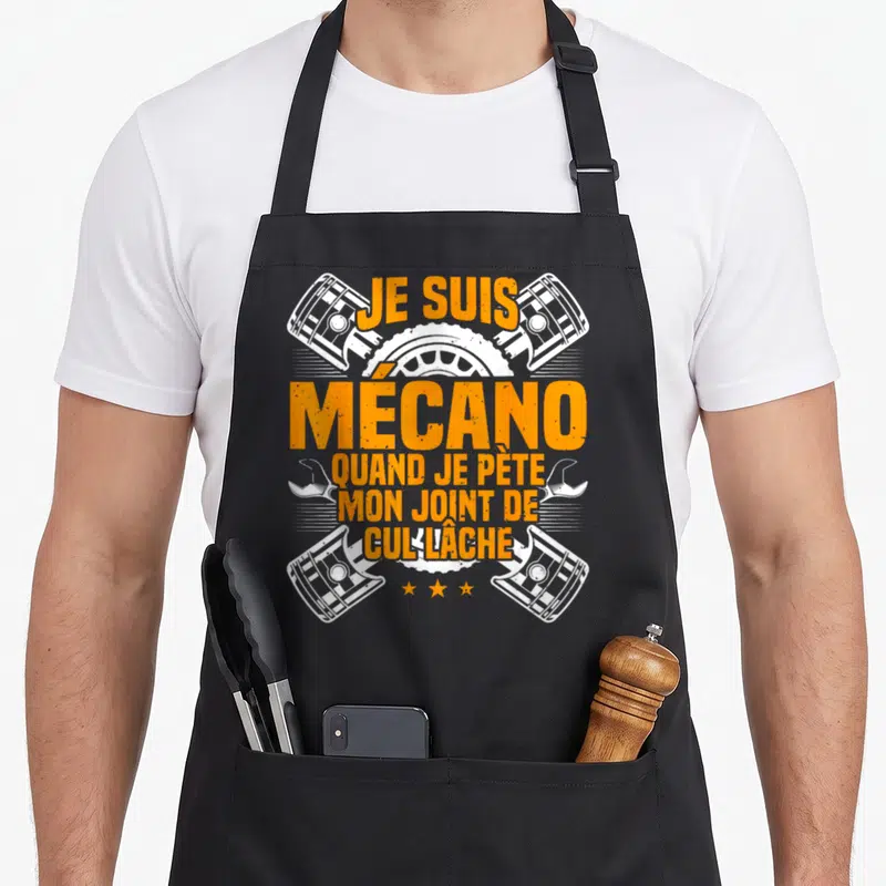 Tablier de cuisine noir avec inscription orange Je suis mécano et illustrations blanches de pistons et clés croisées.