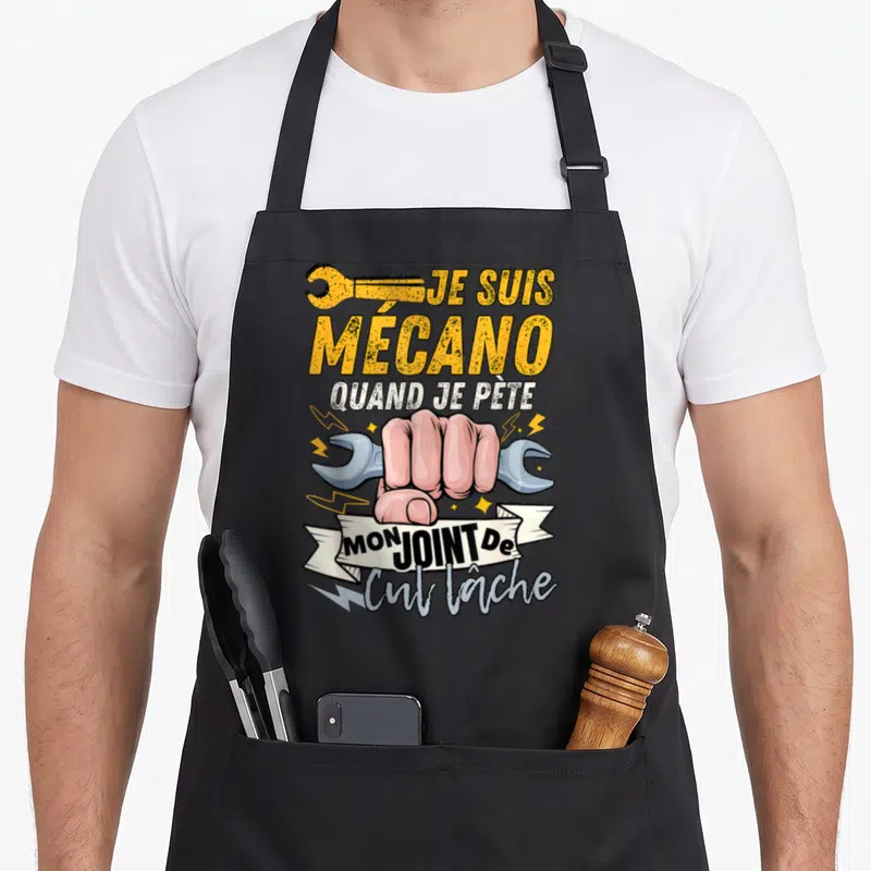 Tablier de cuisine noir avec poing serré tenant une clé à molette et texte humoristique sur la mécanique.