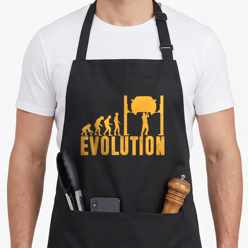 Tablier de cuisine noir avec illustration orange évolution humaine se terminant par un mécanicien sous véhicule sur pont.