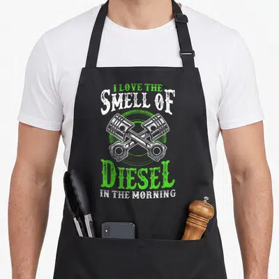 Tablier de cuisine noir avec deux pistons croisés et texte I love the smell of diesel in the morning en vert et blanc.