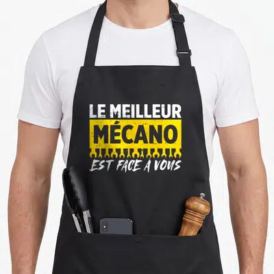 Tablier de cuisine noir avec l'inscription Le meilleur mécano est face à vous et des clés anglaises jaunes en bas du bandeau.