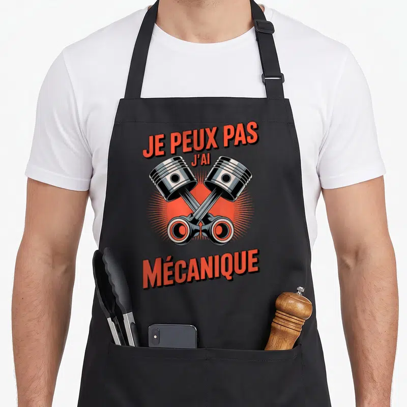 Tablier de cuisine noir avec deux pistons métalliques croisés et texte rouge Je peux pas j'ai mécanique