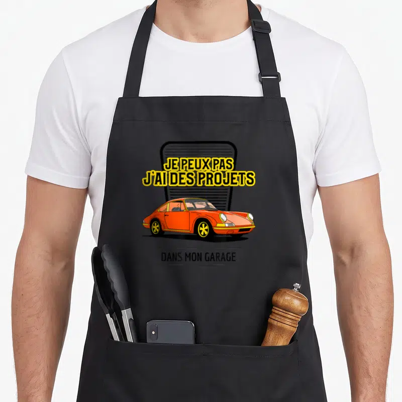 Tablier de cuisine noir avec une voiture orange et le texte Je peux pas j'ai des projets dans mon garage.
