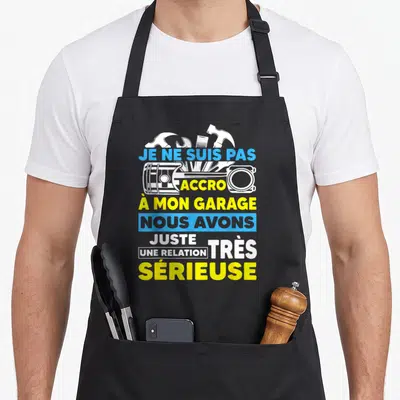 Tablier de cuisine noir avec inscription humoristique sur la passion du garage et des outils mécaniques en bleu et jaune.